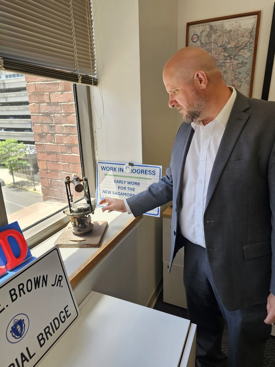 Jonathan Gulliver holding a 20th-century Mass. DPW surveying transit in his office.